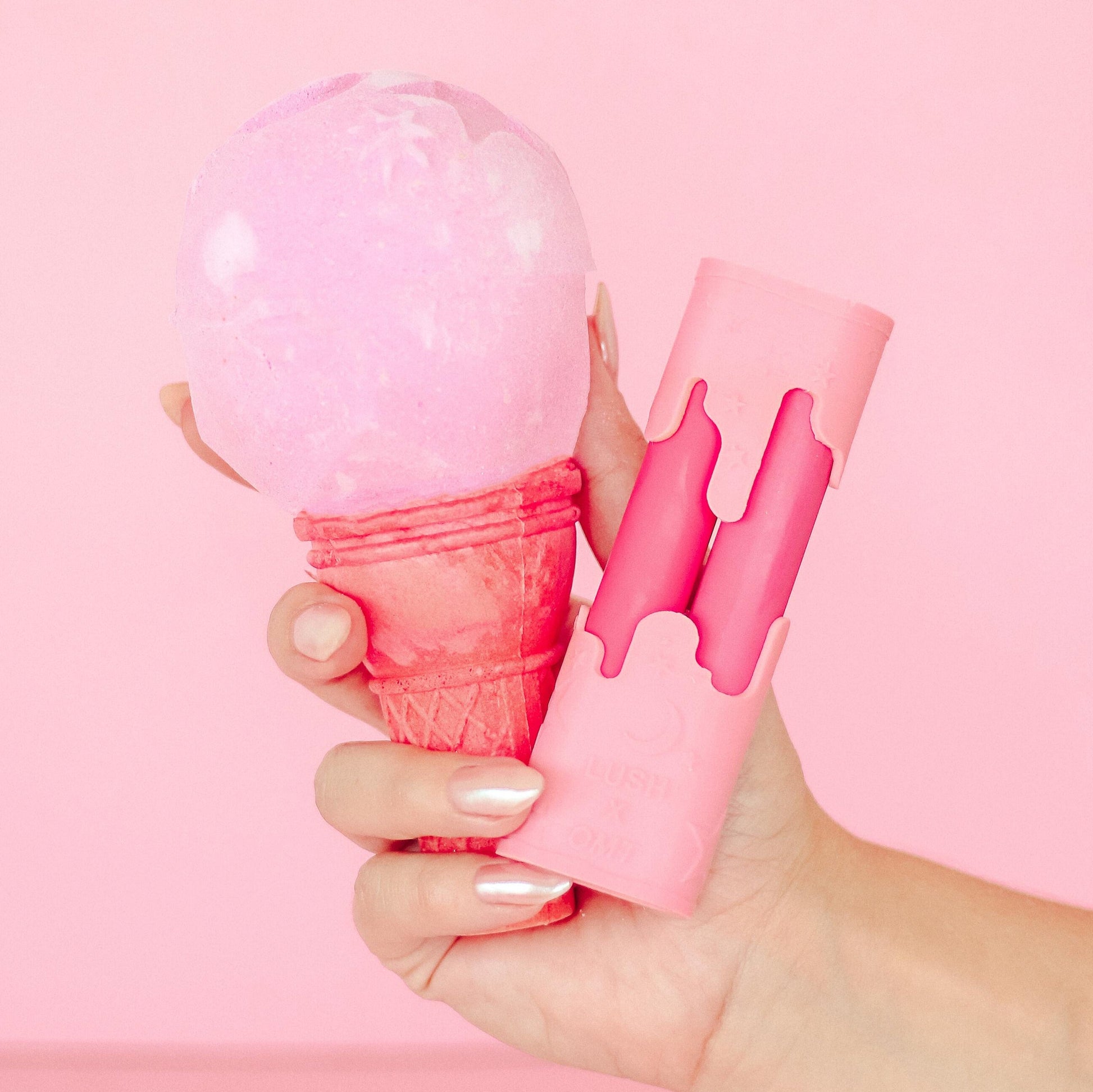 Hand holding a pink ice cream cone with a pink scoop against a pink background